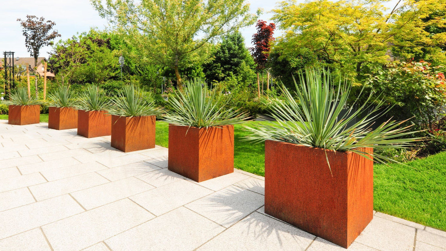 Mehrere quadratische Pflanzkästen Basio aus Cortenstahl mit Edelrost auf einer Terrasse