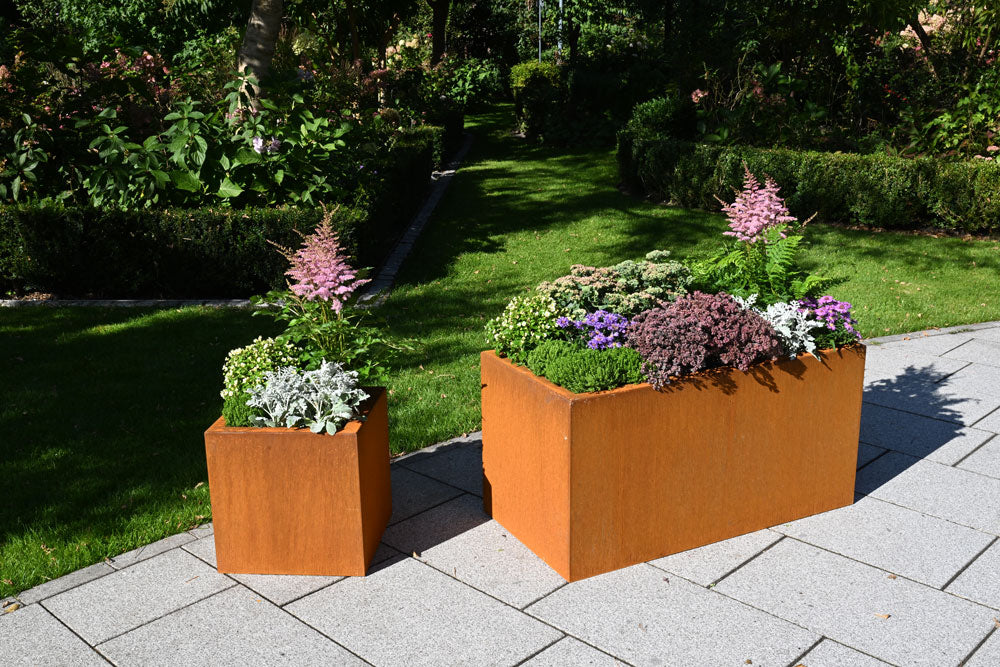 Corten Pflanzkästen Basio quadratisch und rechteckig mit Blumen auf der Terrasse vorm Garten